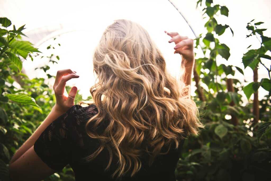 Blonde woman with curly hair surrounded by lush greenery, enjoying a sunny day.